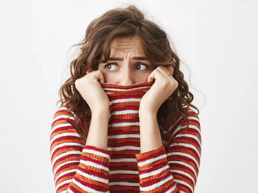 Mujer con expresión de temor y timidez cubriéndose parte del rostro con su jersey, representando la sensación de inseguridad.