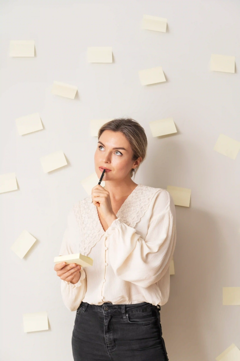 Mujer joven pensativa frente a una pared llena de notas adhesivas, representando la saturación mental y la dificultad para tomar decisiones.