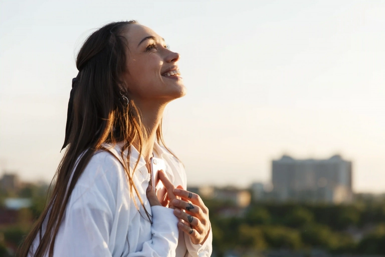 Una mujer joven con una expresión de alivio y serenidad, mirando hacia el cielo y conectando con sus emociones positivas, simbolizando el proceso de sanación emocional.