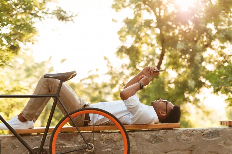 Hombre joven descansando con su bicicleta pero usando el móvil